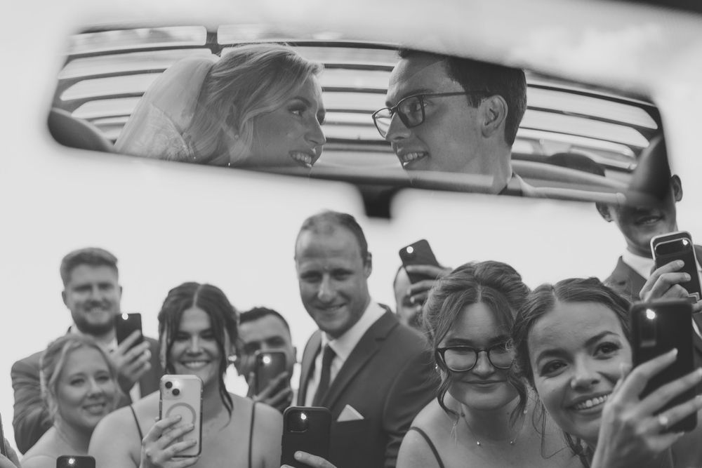 A large group of people smiling and taking selfies together at an outdoor gathering.