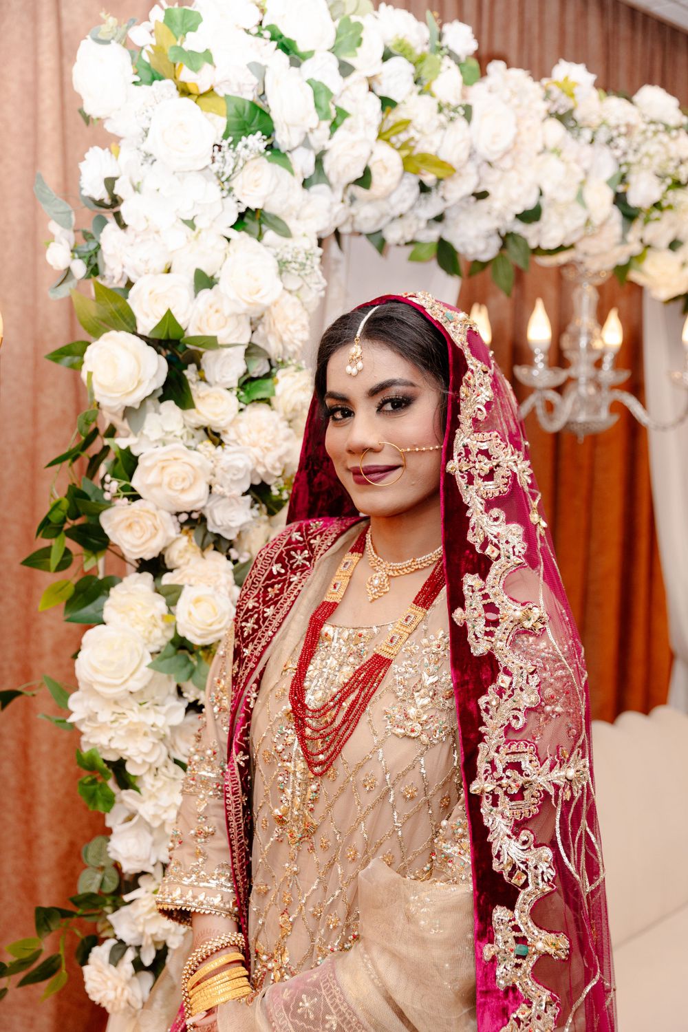A bride in a red and gold bridal dress posing in front of a floral arrangement.