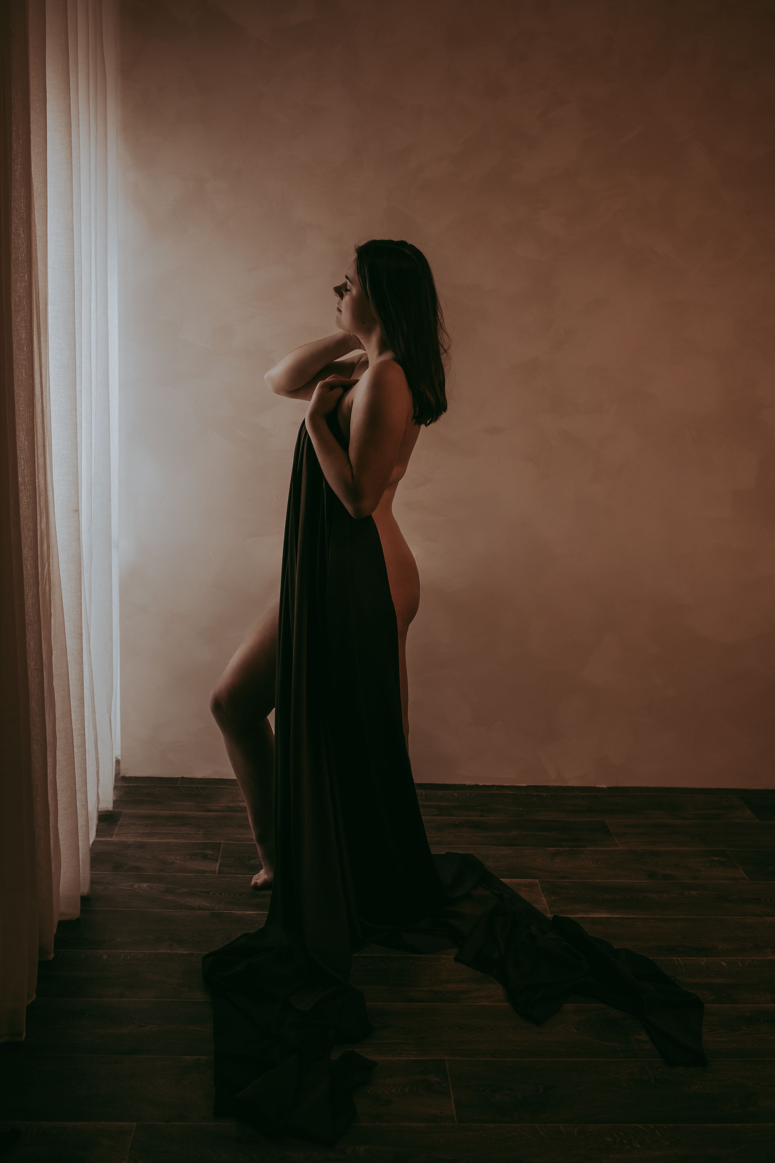 Elegante vrouw met een kleed gedrappeerd voor haar lichaam kijkend uit het raam