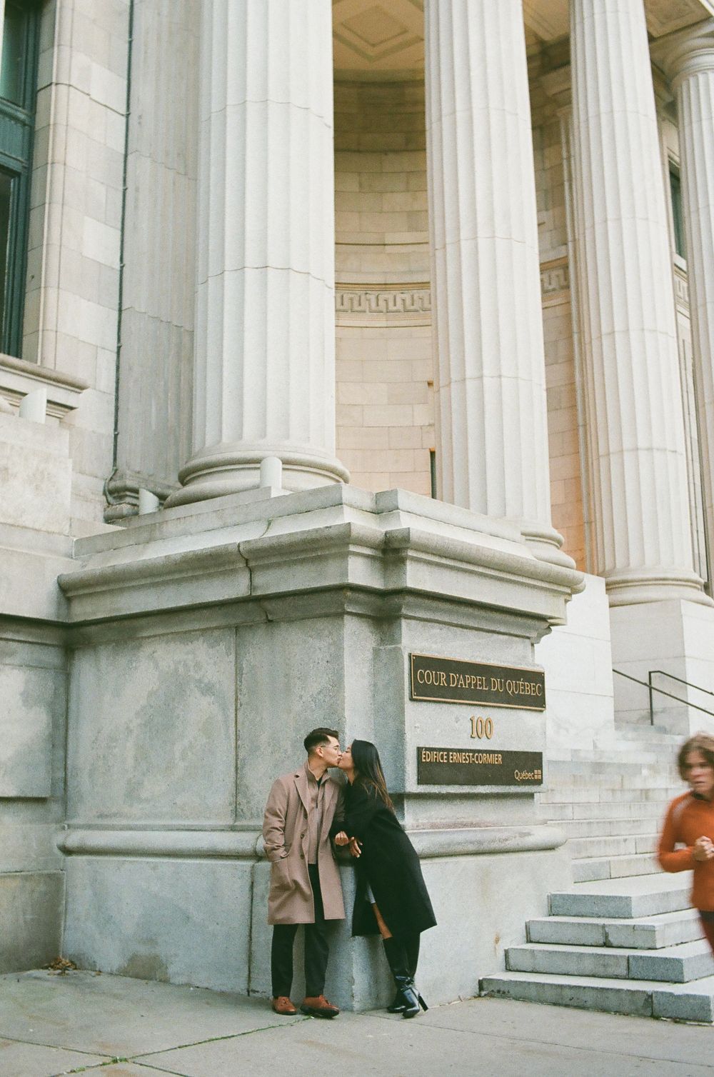 Couple sharing a romantic kiss beside a grand stone column at Cour d'Appel du Quebec courthouse. 35mm film photoshoot