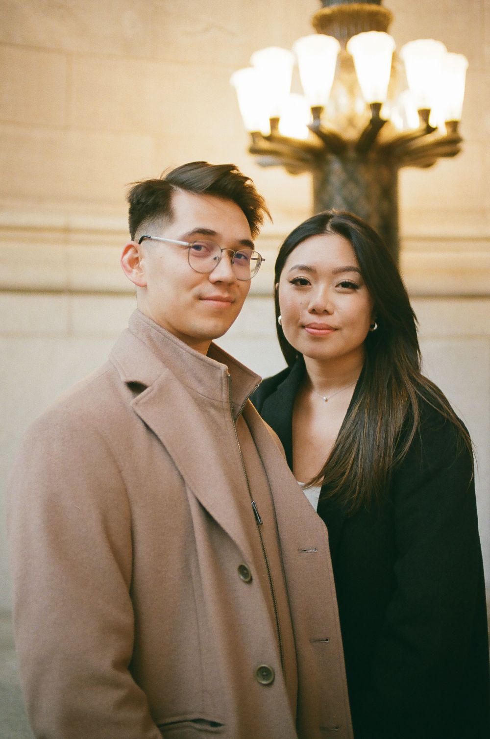 Young Asian couple posing together under a vintage street lamp in warm golden light. Aliza's Dworkind engagement film photographer