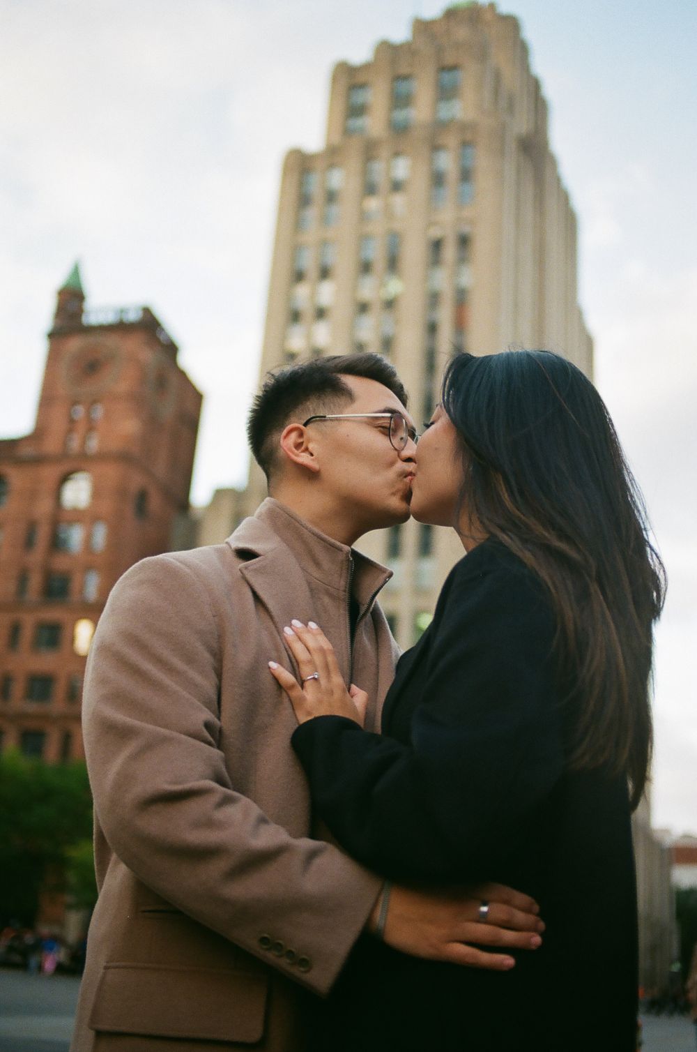 Couple sharing a kiss outdoors with historic urban buildings visible in the background. Old Port Montreal photographer.