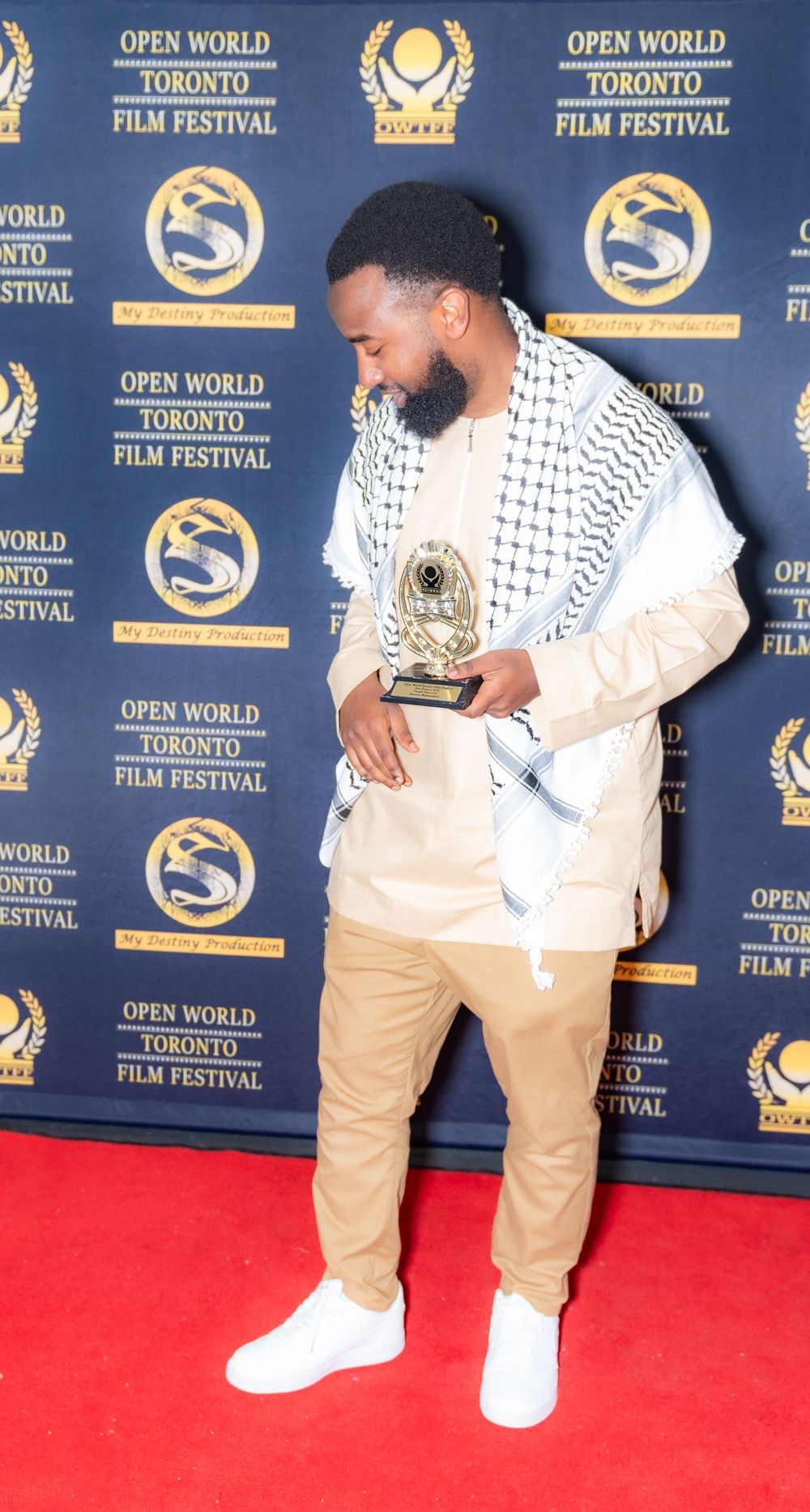 Award recipient at Open World Toronto Film Festival holding trophy on red carpet.