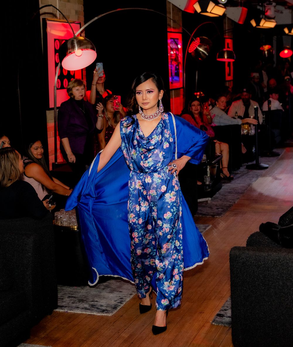 Model showcasing blue floral evening wear on illuminated runway with audience.