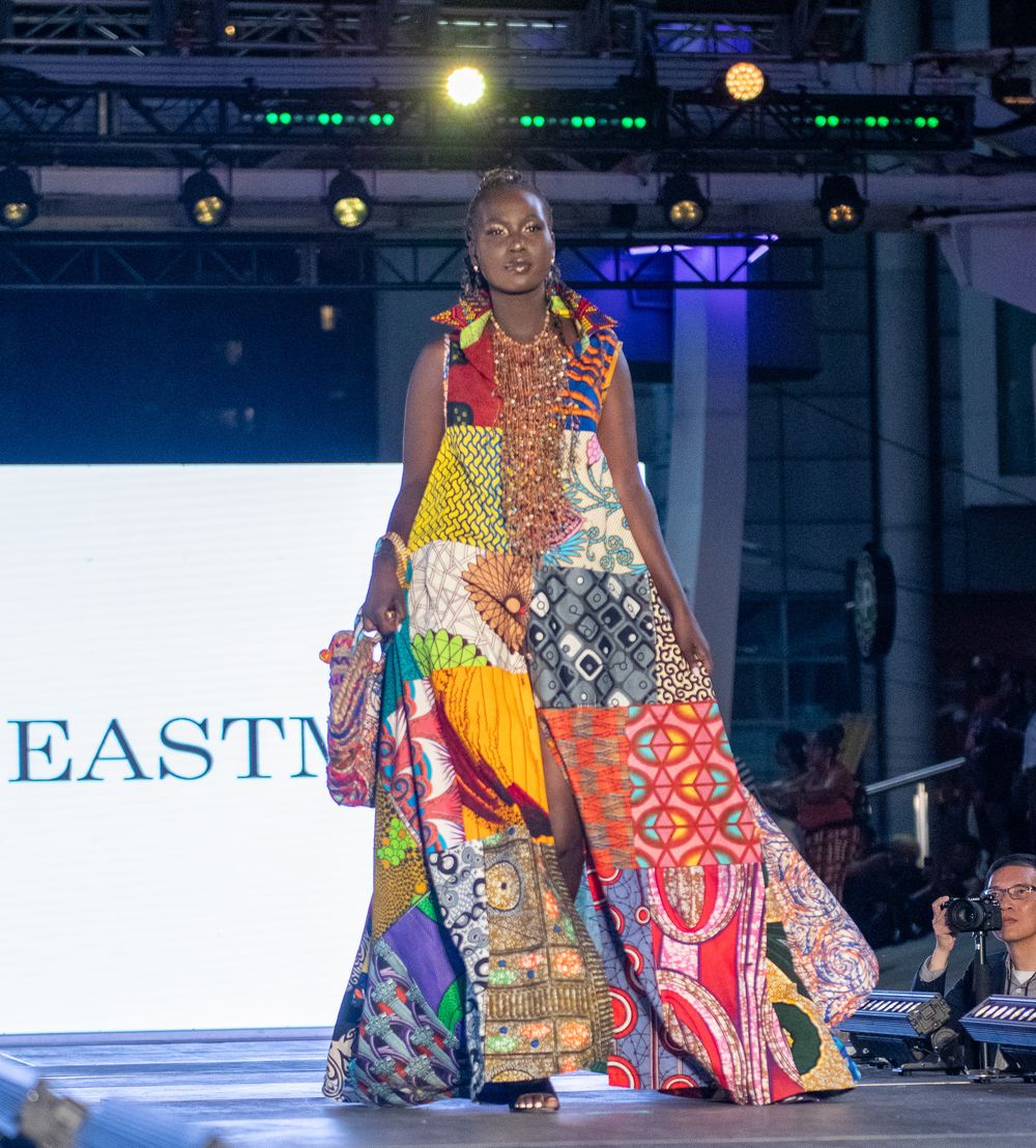 Runway model wearing colorful patchwork dress with mixed patterns and prints.