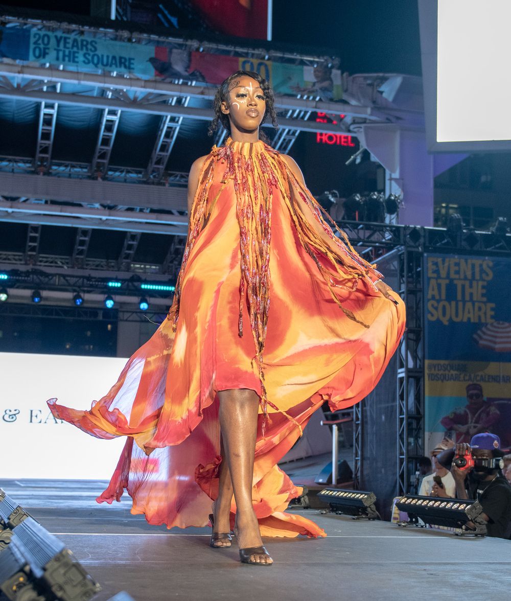 Model showcasing flowing orange gown with dramatic movement on fashion runway.