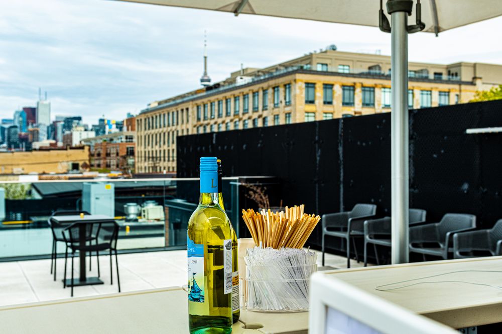 Rooftop dining area with wine bottle and umbrella against urban skyline backdrop.
