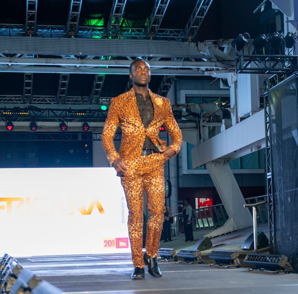 Model wearing bright orange patterned suit on illuminated fashion runway.