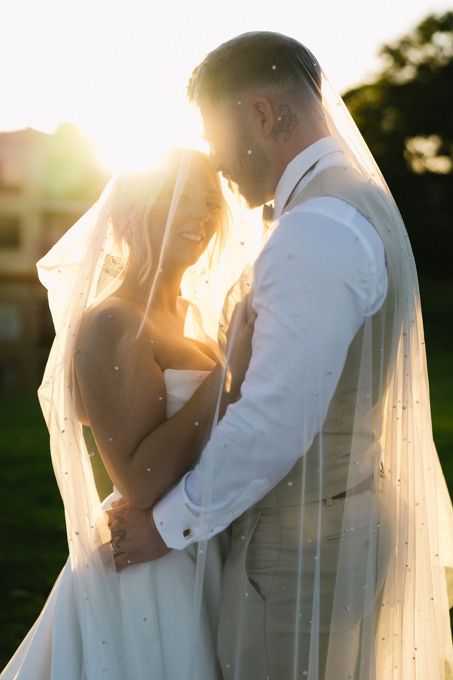 Bride and groom share a romantic kiss surrounded by guests holding sparklers at their outdoor nighttime wedding celebration.