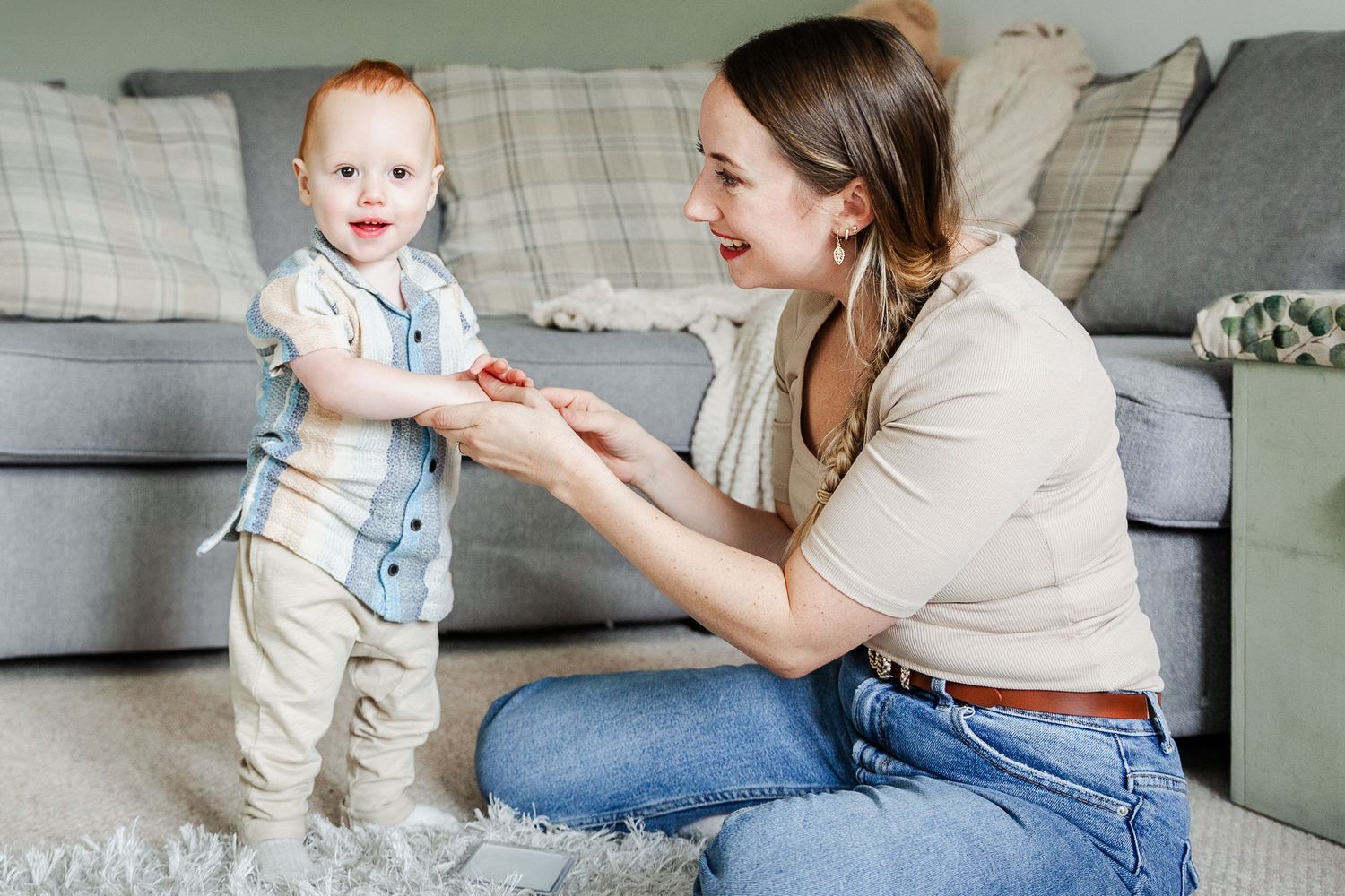 A toddler stands and looks to camera as he holds his mum's hands during a relaxed and unposed photoshoot at home. Bristol baby photographer