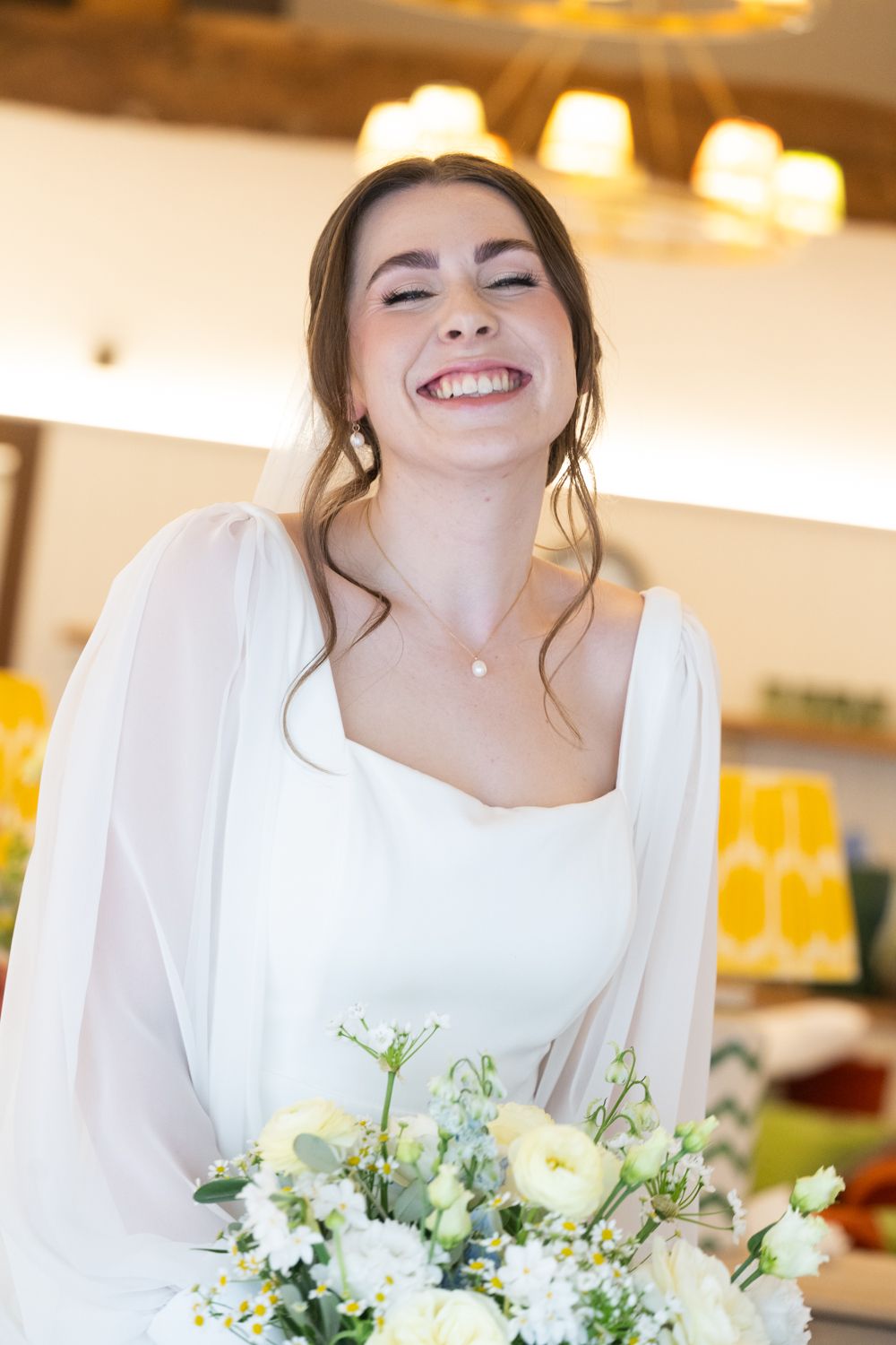 Joyful bride in white dress laughing while holding bouquet of white flowers at wedding ceremony.