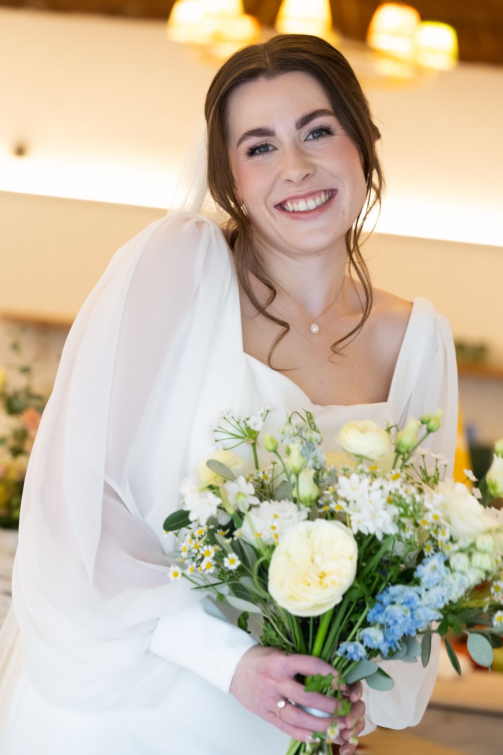 Smiling bride in white dress holding a bouquet of yellow, blue, and white flowers on her wedding day.
