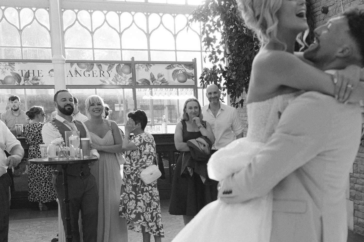 Black and white wedding photo of couple embracing on dance floor while guests watch and celebrate in elegant venue.