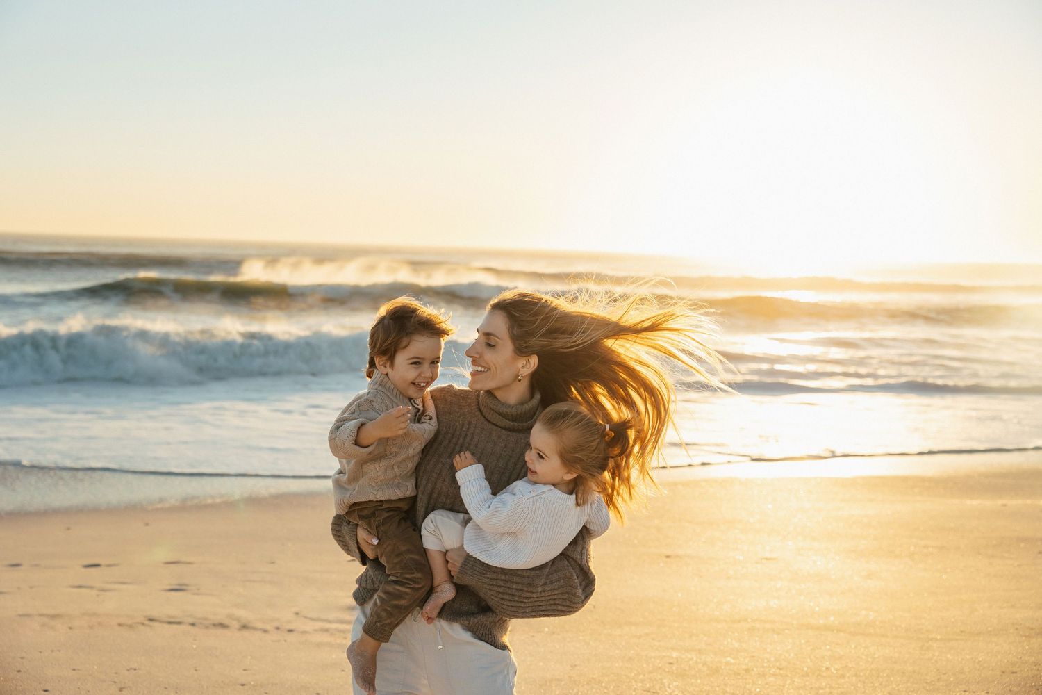 mother dancing with her children at the beach with golden light