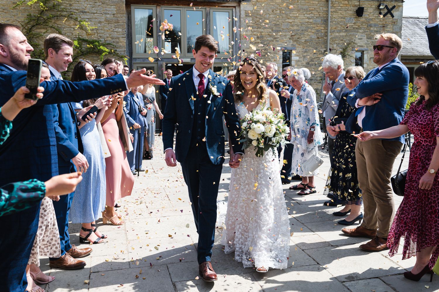 Bride and groom walking through a joyful confetti shower at Caswell House Wedding Venue surrounded by cheering wedding guests.