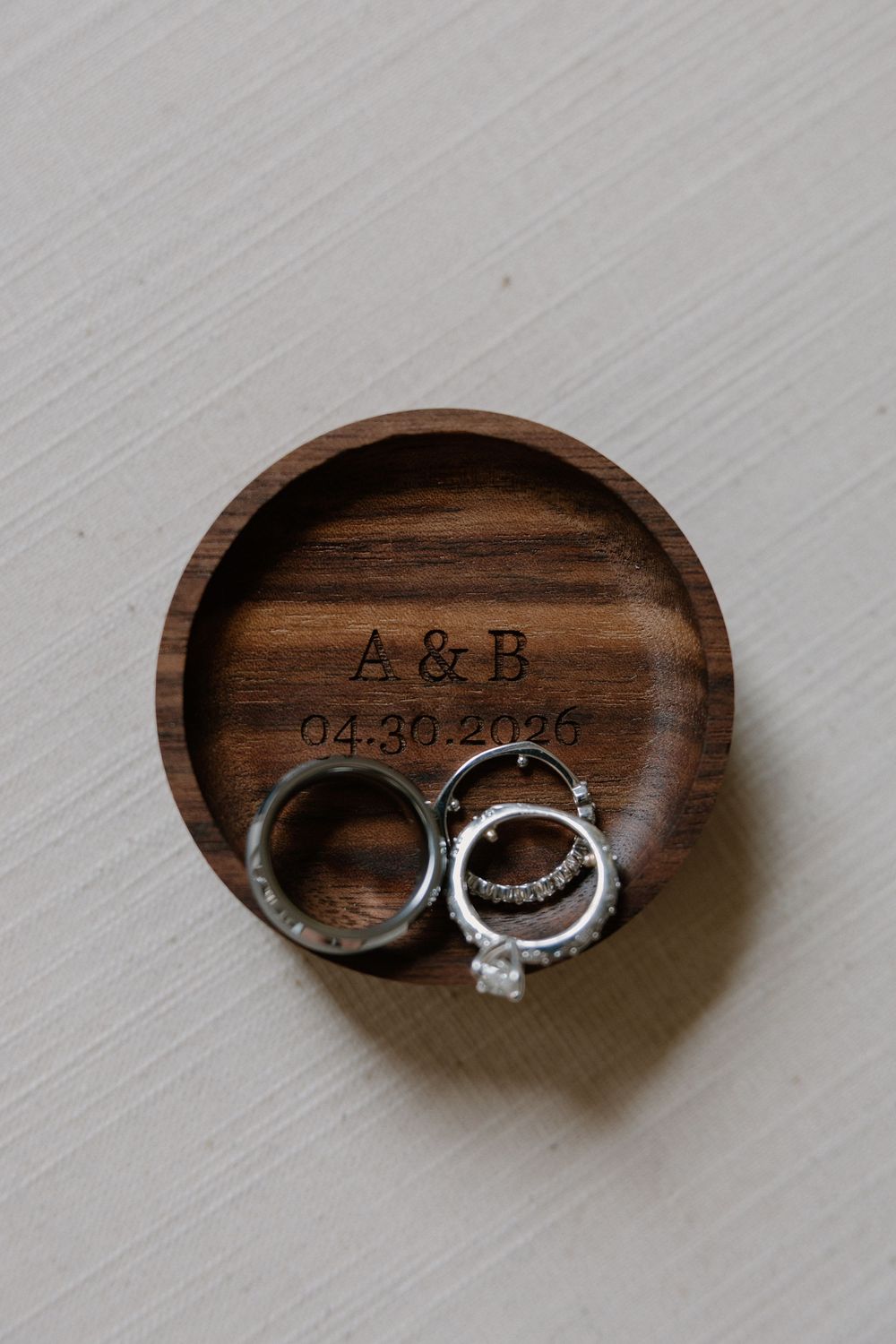 Wedding rings and engagement ring displayed in a personalized wooden ring dish engraved with A&B and date 04.30.2026.
