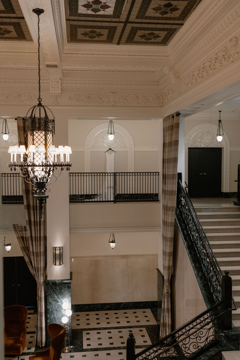 Grand hotel lobby featuring ornate coffered ceiling, crystal chandelier, marble floors, and elegant wrought iron staircase.