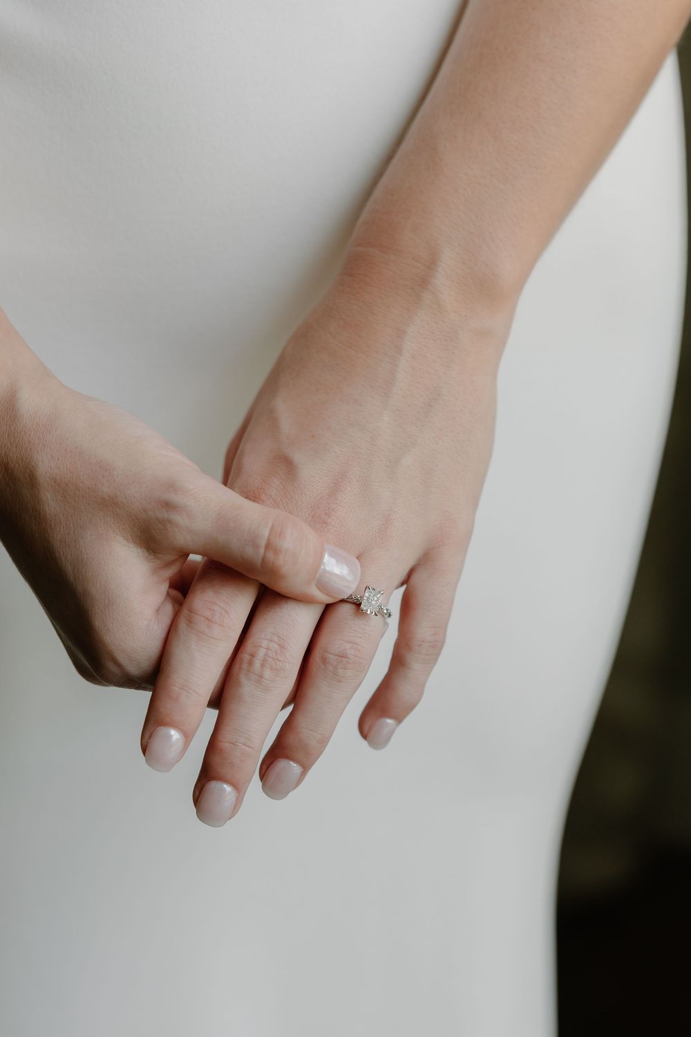 Close-up of bride and groom holding hands showing a sparkling diamond engagement ring on wedding day.