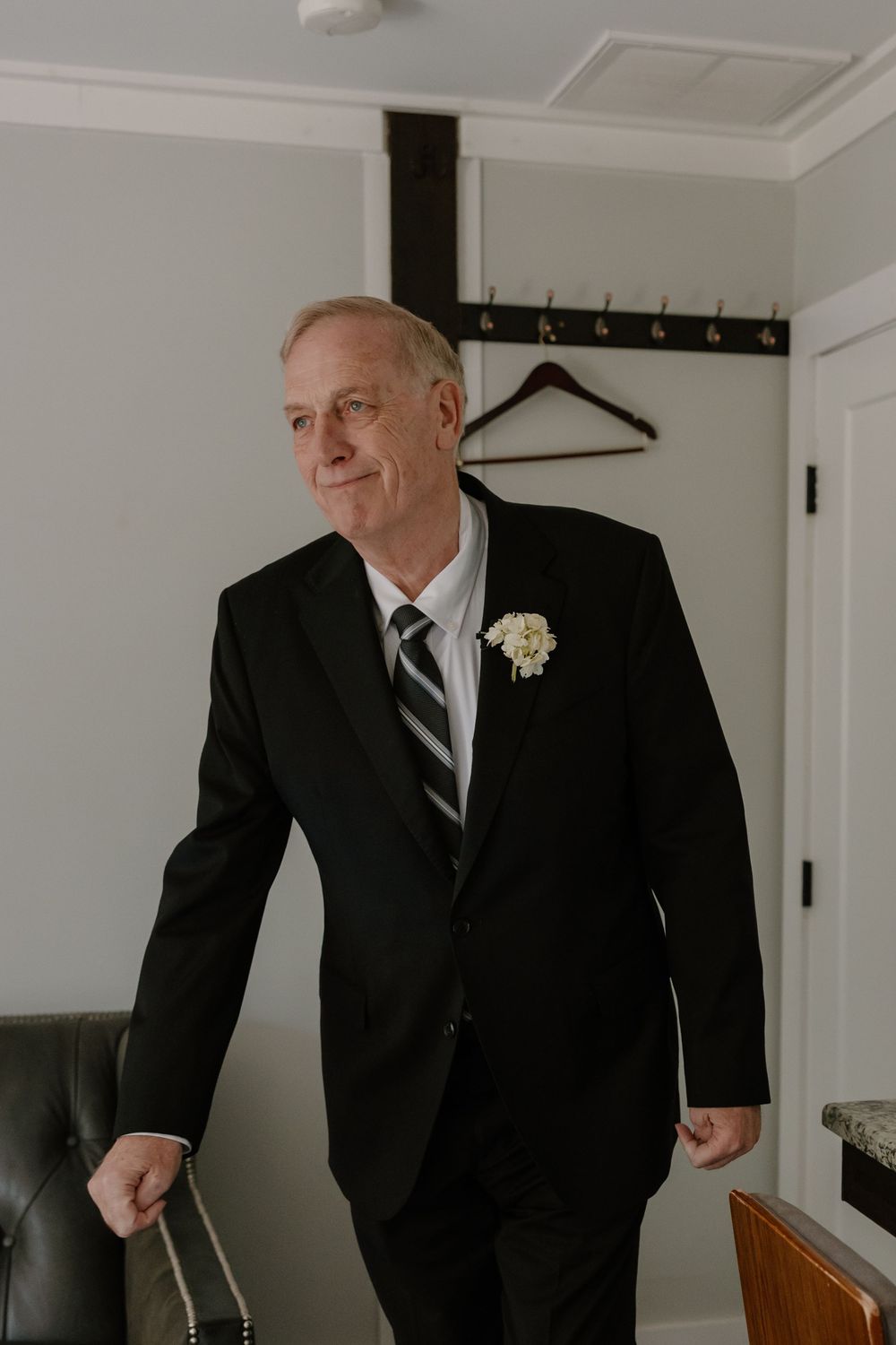 Dapper older gentleman in black suit with floral boutonniere smiling at a wedding celebration.