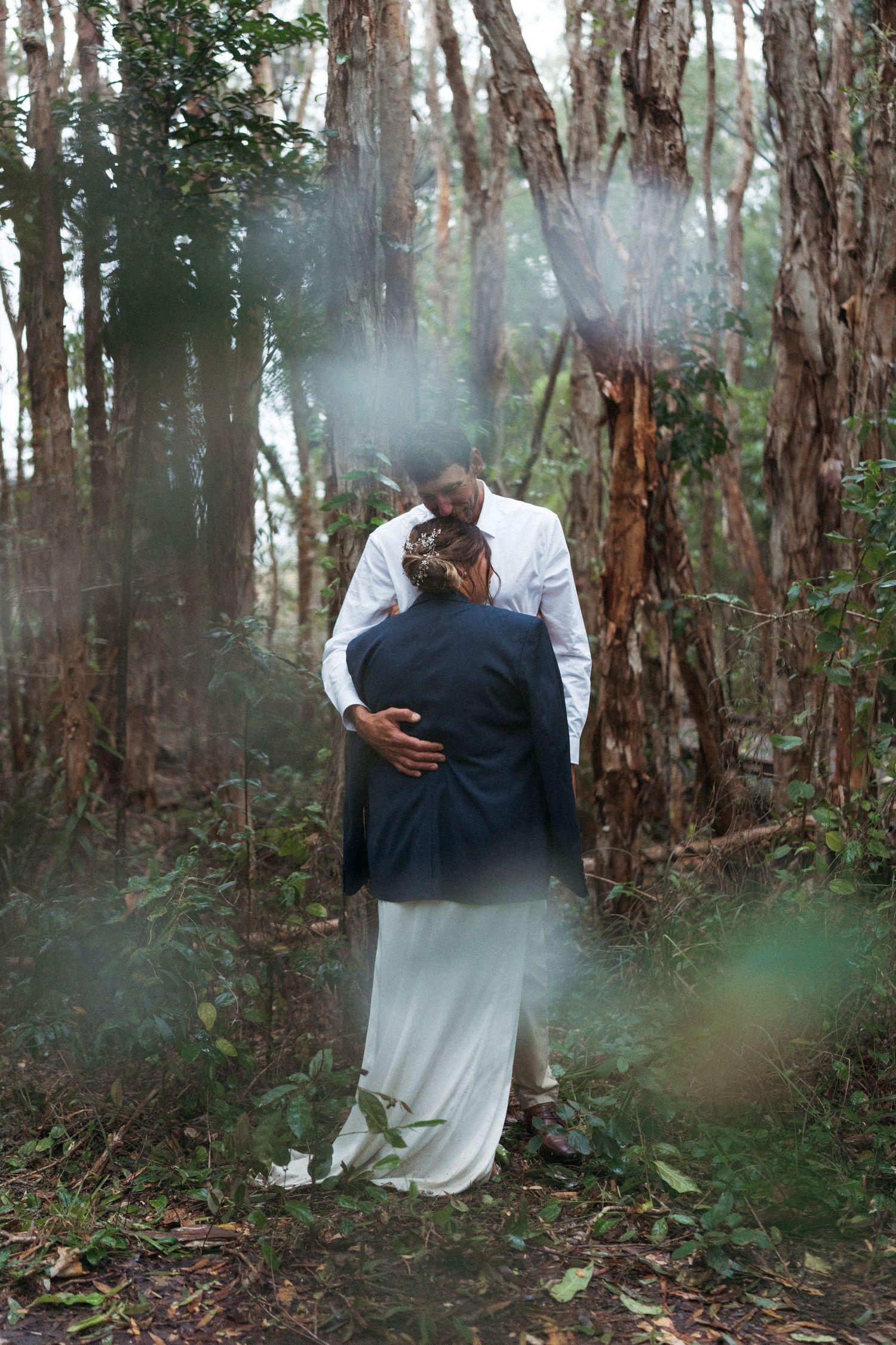 Bride and groom sharing a romantic kiss in a lush forest pathway on their wedding day in the paperbark trees Rainbow Beach.