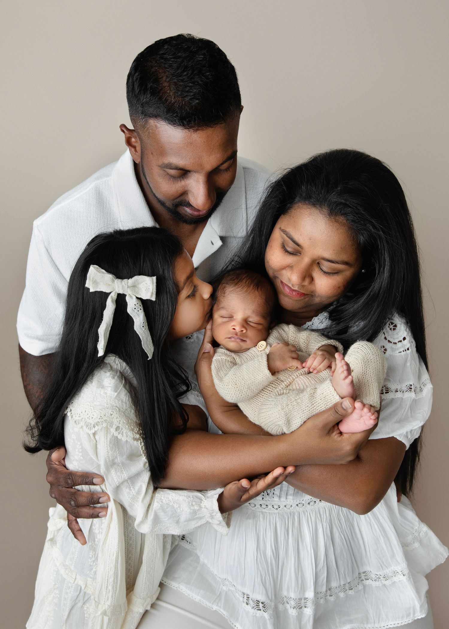 Parents tenderly hold their newborn baby together, touching foreheads in an intimate family portrait.