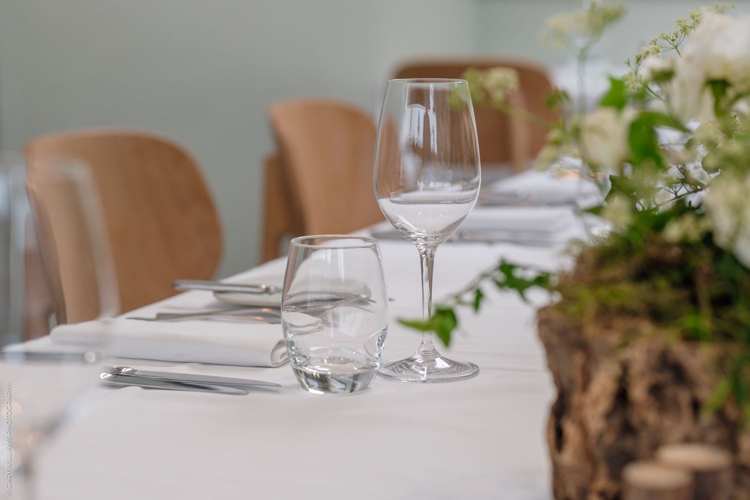Elegant restaurant table setting with crystal wine glasses, white linen napkins, and floral centerpiece.