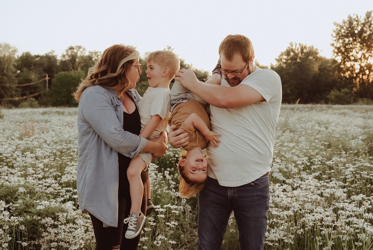 Family playfully interacting in a field of white wildflowers at sunset.