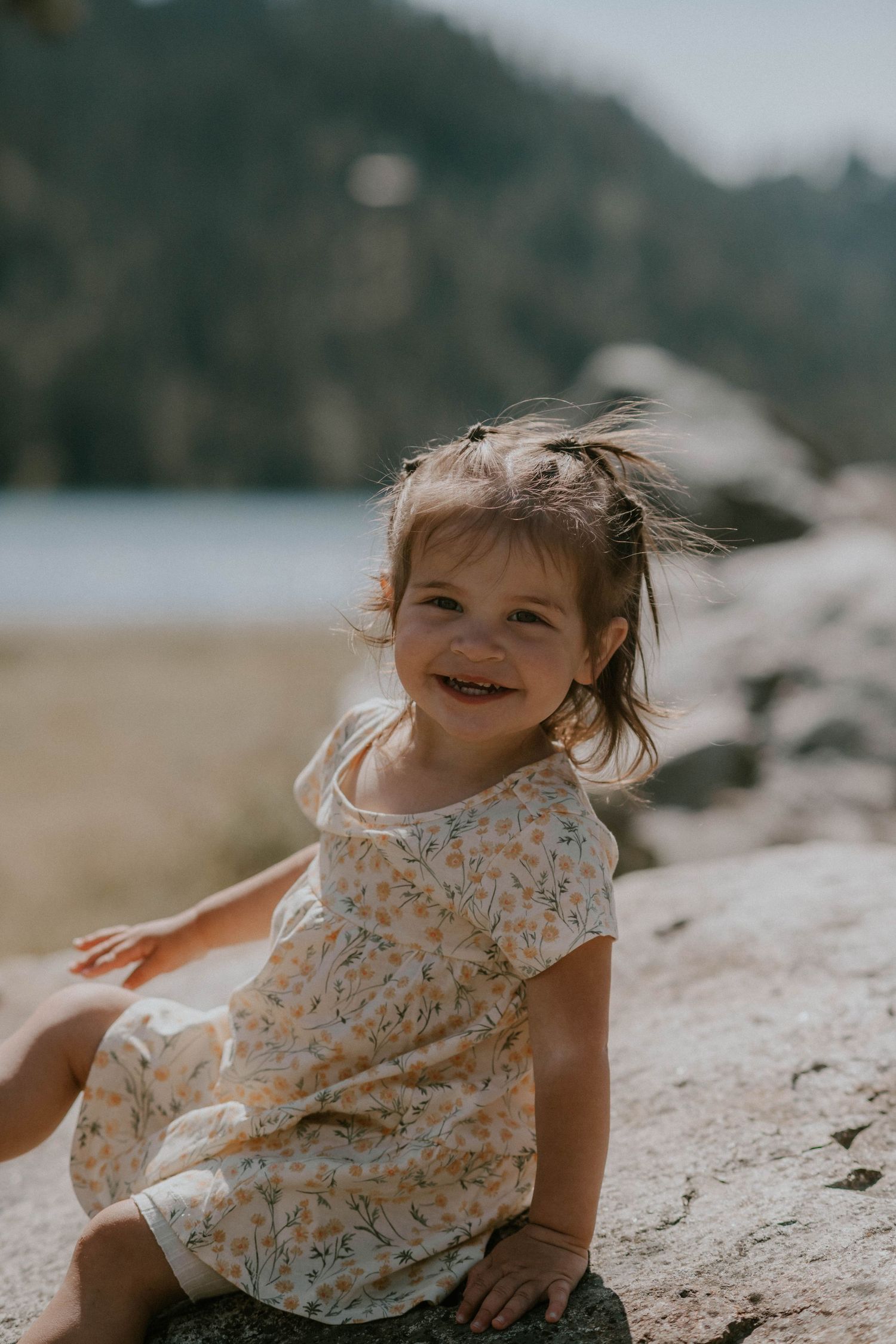 A smiling man in a white t-shirt carries a happy little girl on his shoulders outdoors with hills in the background.