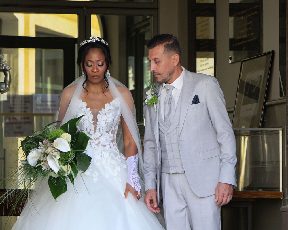 Bride in white ball gown with veil and groom in light gray suit walking together at an outdoor wedding venue.