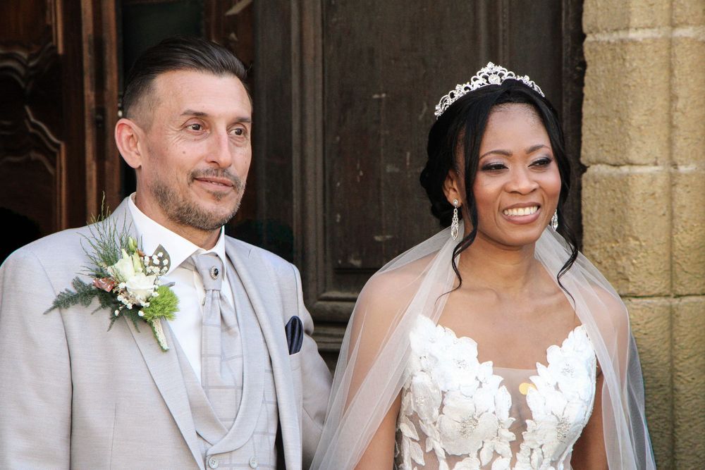 Happy interracial couple in wedding attire, groom in gray suit and bride in white lace gown with tiara and veil.