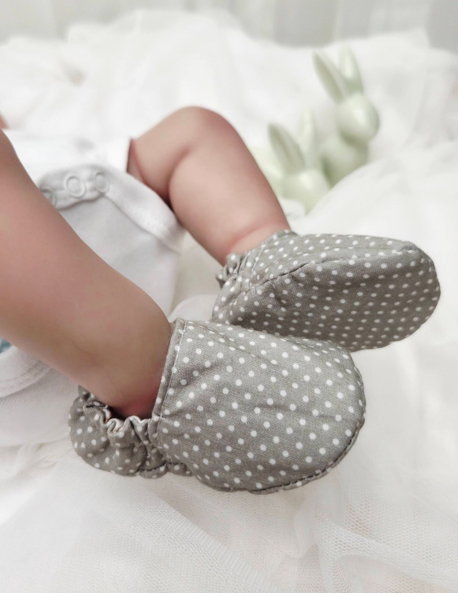 Adorable gray polka dot baby booties on tiny infant feet, soft fabric with elastic ankles on white background.