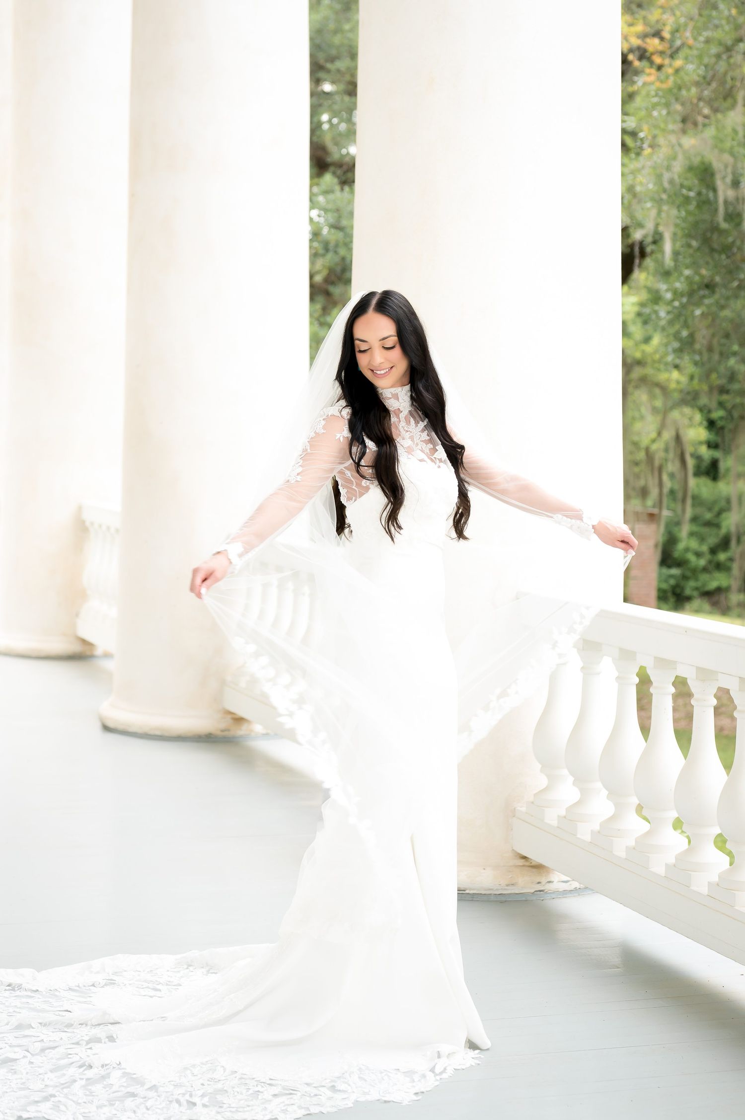Bride in elegant white lace long-sleeve wedding gown twirling on a grand white columned veranda.