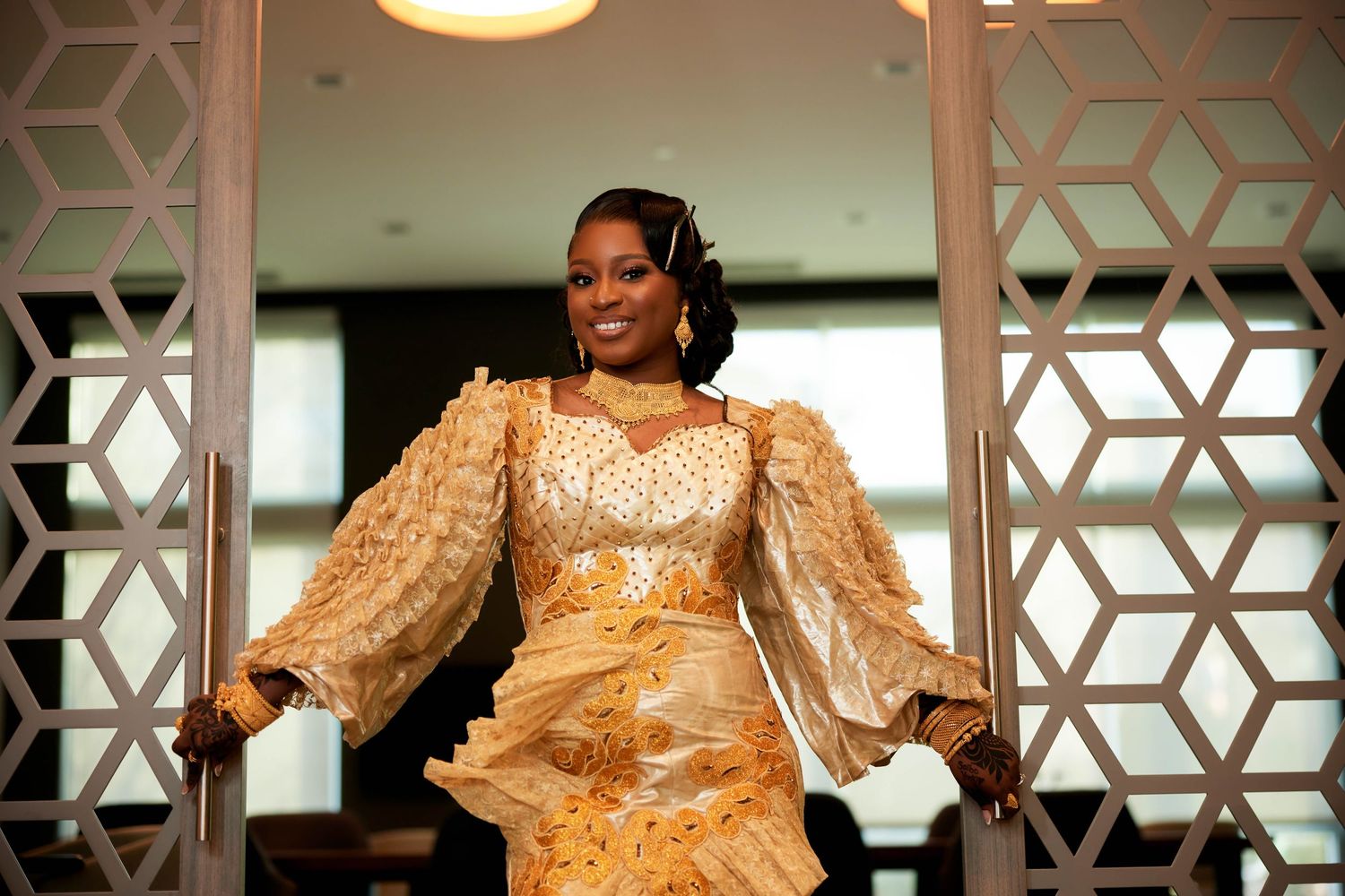 Woman in elegant gold African traditional dress with puff sleeves posing gracefully at a formal event.