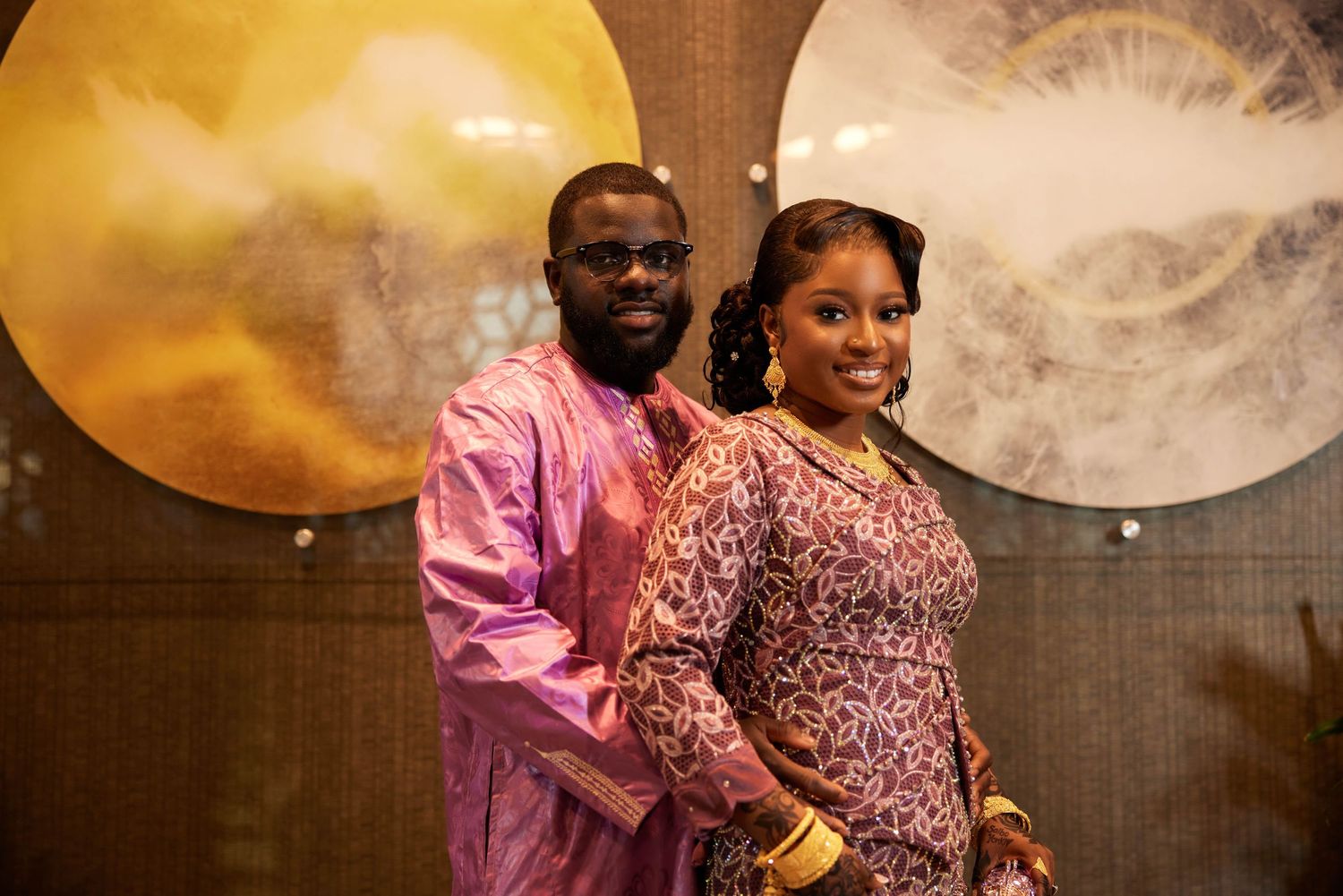 Couple in matching pink and gold traditional African attire posing together at a formal celebration.