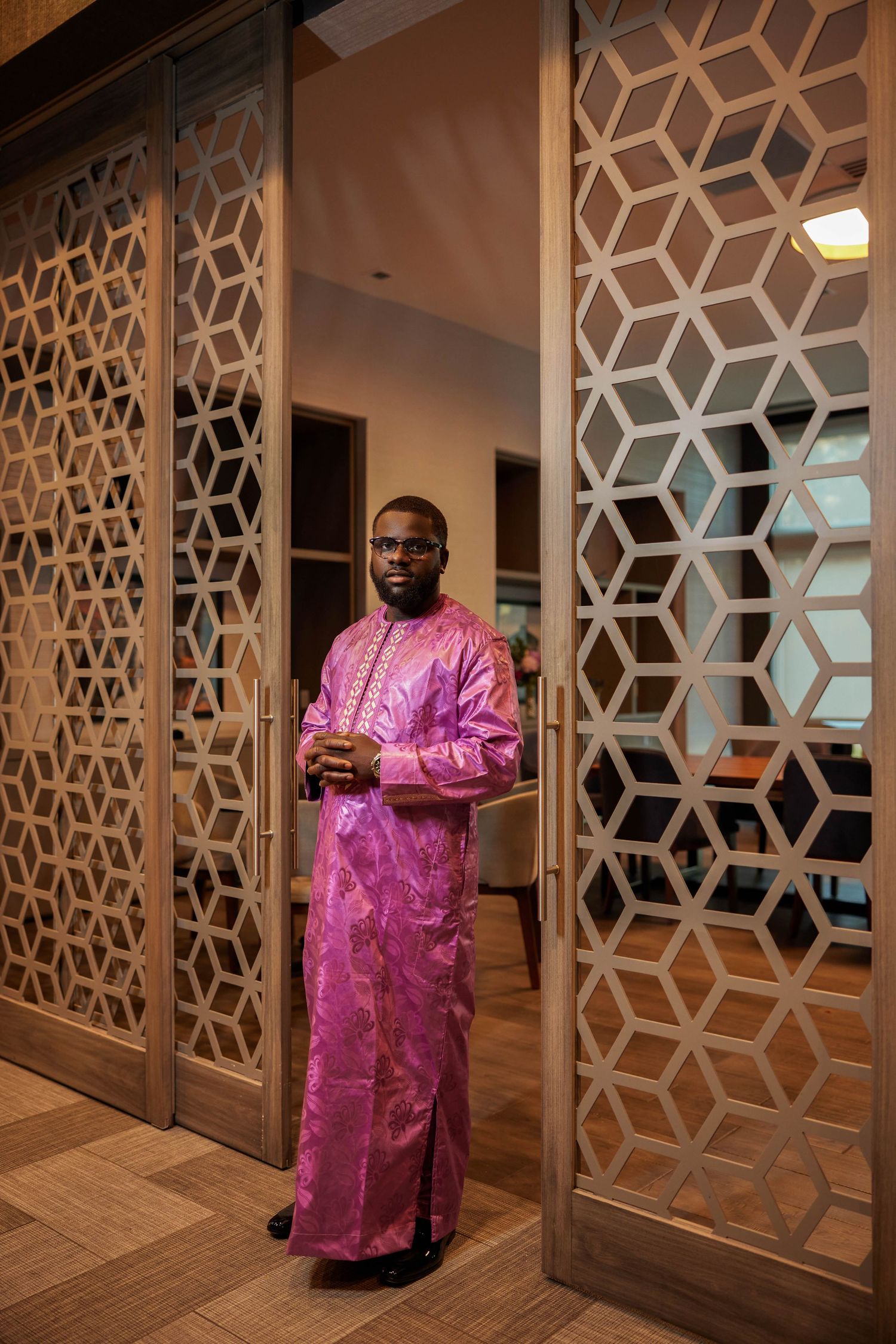 Man in vibrant purple African traditional attire standing in decorative doorway with geometric lattice panels.