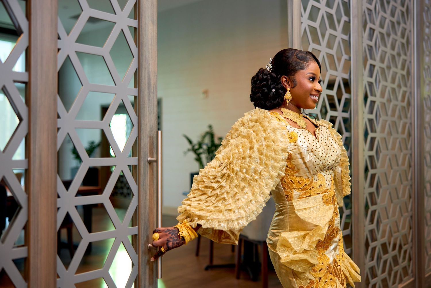 Woman in elegant gold African dress opening decorative geometric door.