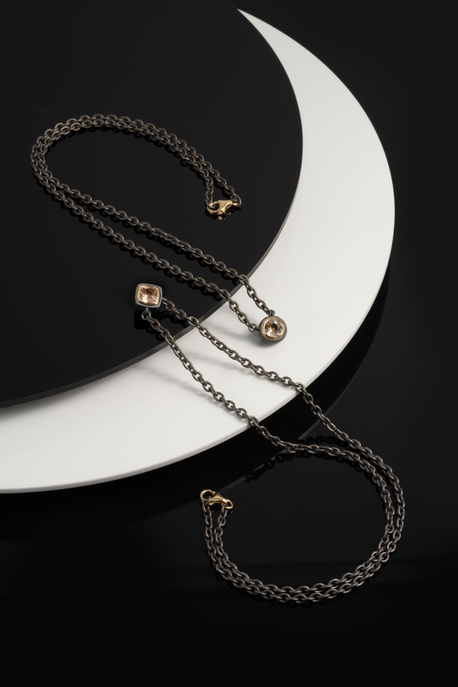 Dark oxidized silver chain necklace with crystal pendants displayed on a black and white circular prop.