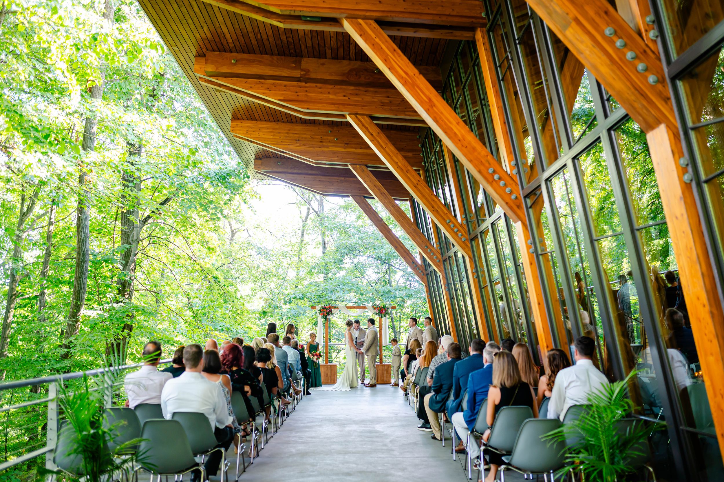 Outdoor wedding ceremony in a stunning wooden pavilion surrounded by lush green forest trees.