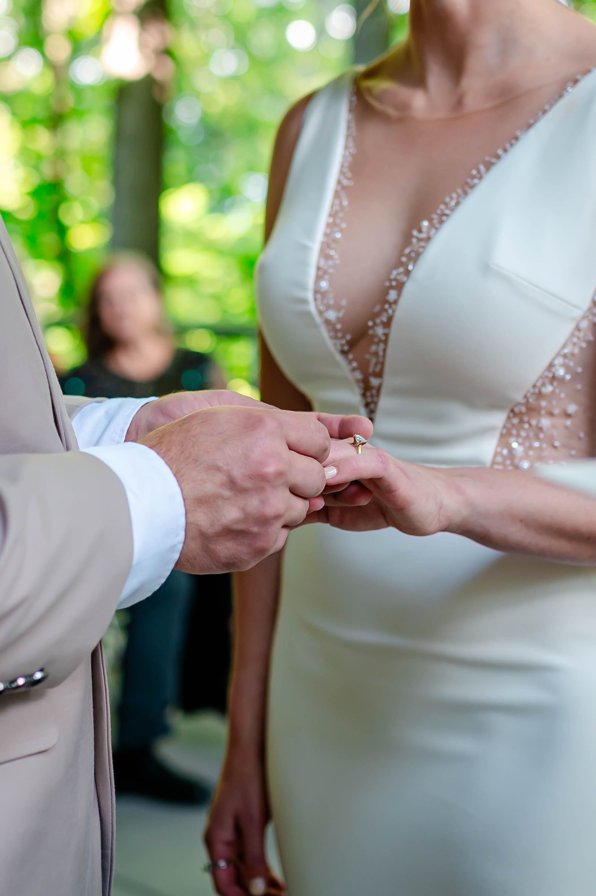 Groom placing a wedding ring on bride's finger during outdoor ceremony, bride wearing elegant white beaded gown.