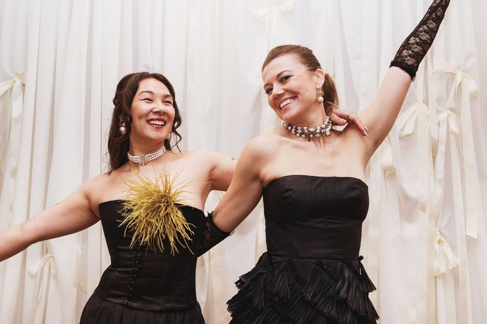 Two women in black strapless dresses smiling and posing together at a formal event.