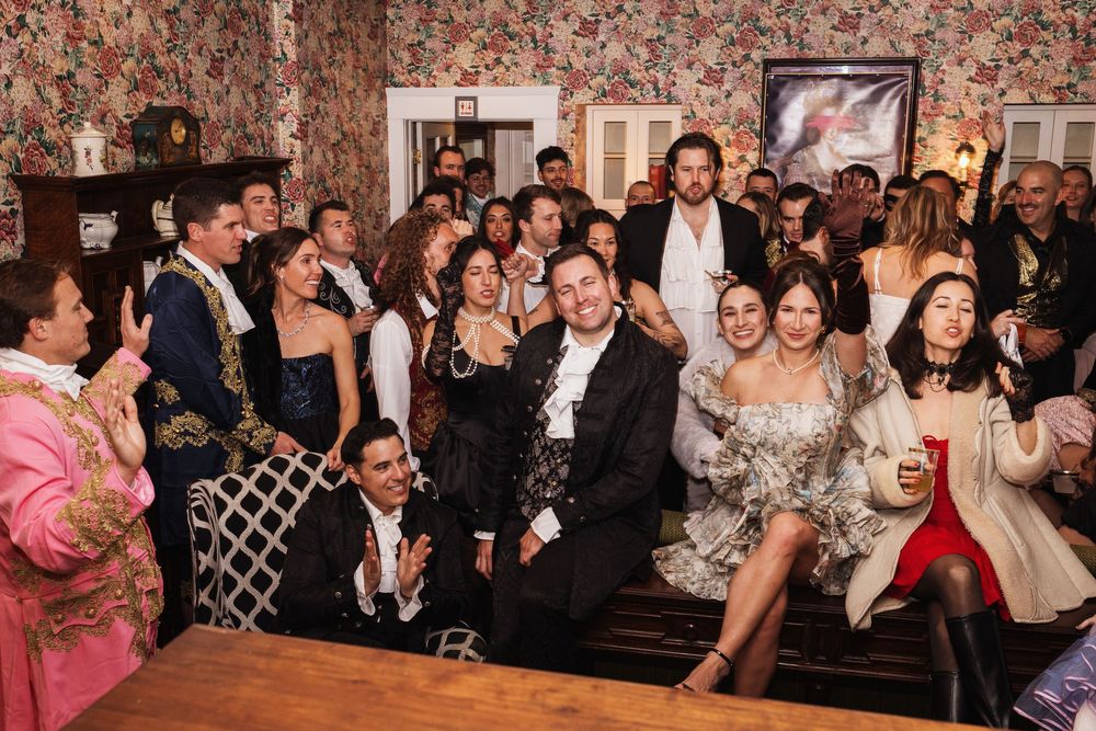 Large group of elegantly dressed guests posing together at a festive costume party in a decorated indoor venue.