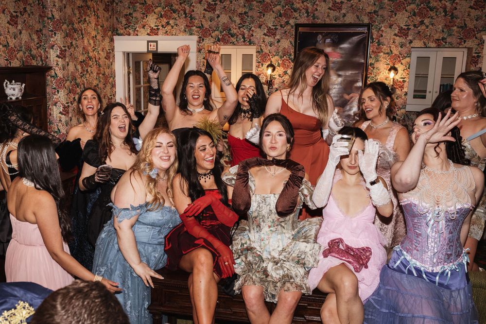 Group of women in elegant dresses celebrating joyfully at a lively indoor party event.