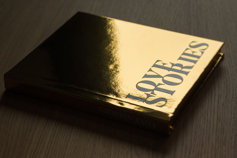 Gold metallic hardcover Love Stories photo book lying flat on a dark surface.