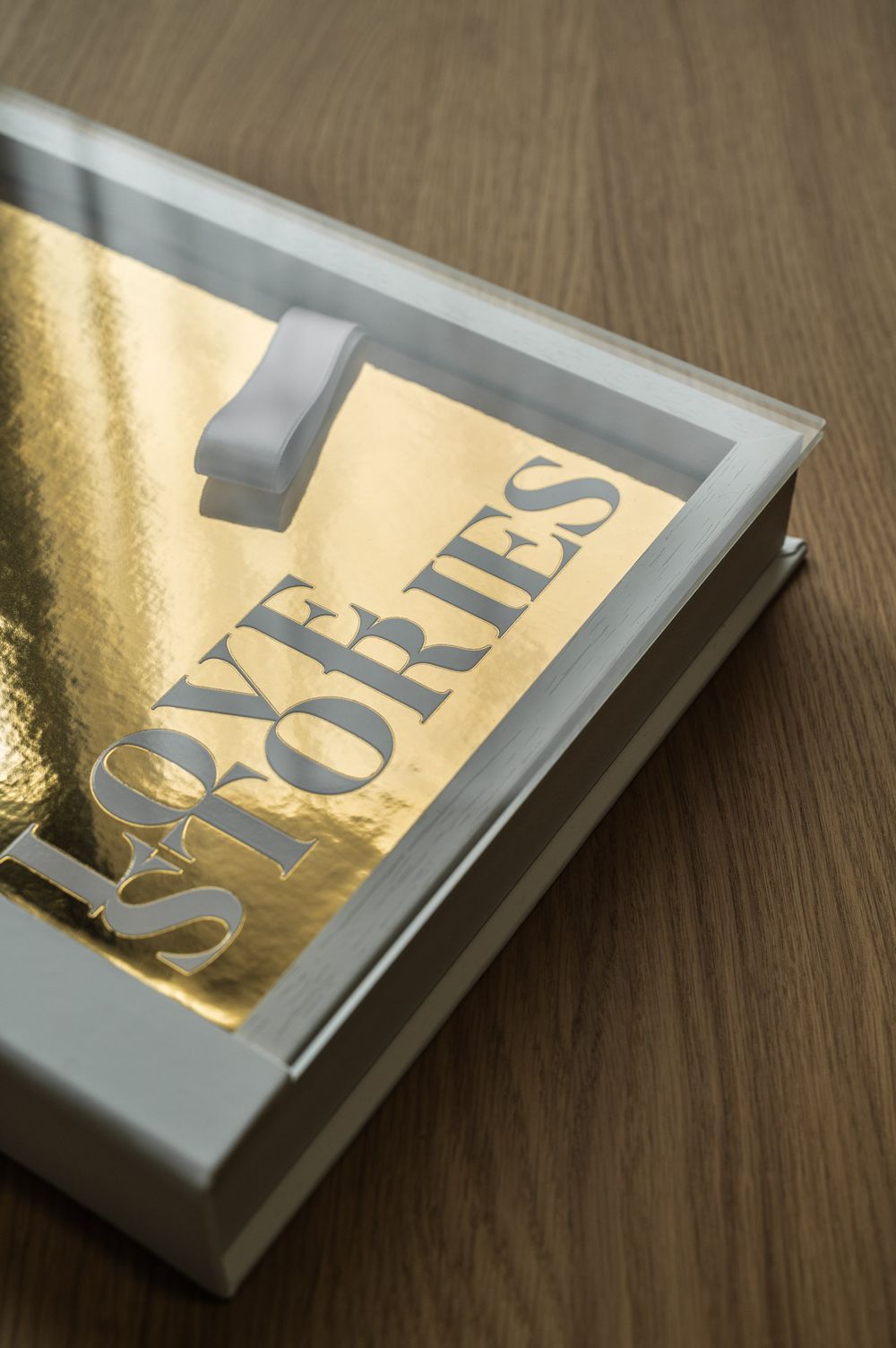 Gold Love Stories photo book inside a white acrylic display box on a wooden surface.