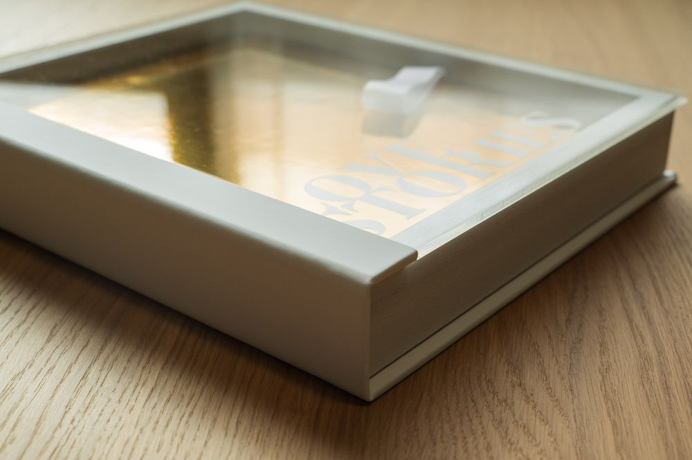 Corner detail of a white acrylic presentation box containing a gold photo book.