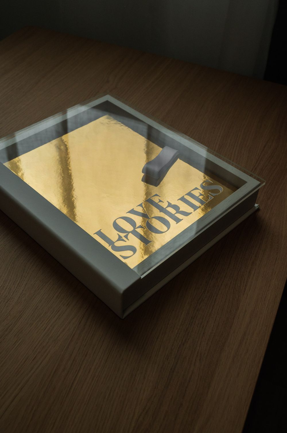 Gold metallic Love Stories photo book inside a white acrylic keepsake box on a dark surface.