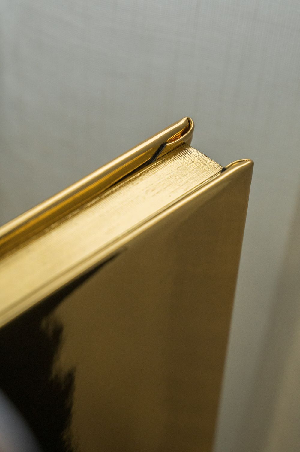 Side view of a shiny gold hardcover photo book standing upright against a light background.