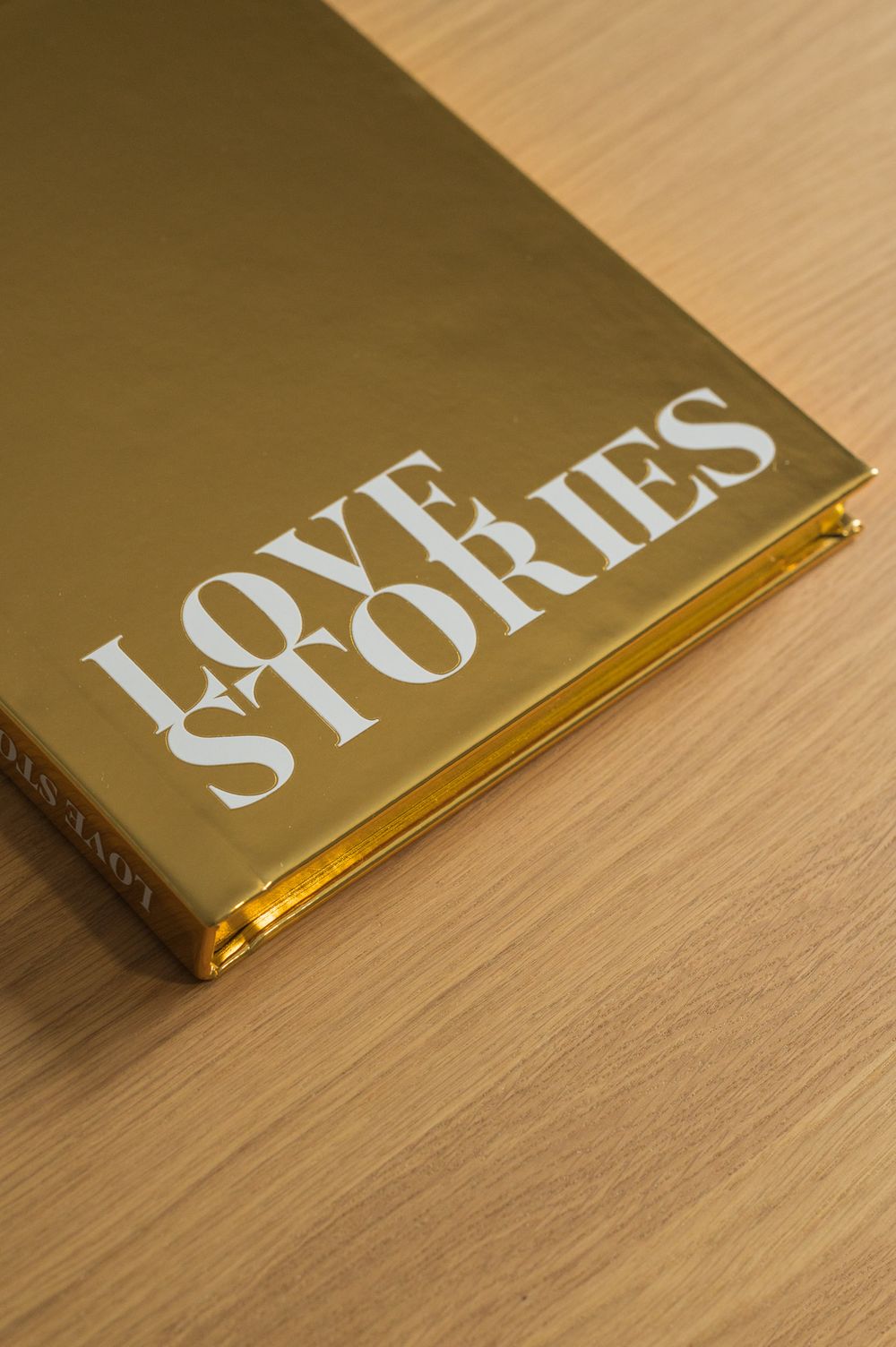 Gold metallic hardcover photo book titled Love Stories lying flat on a wooden surface.