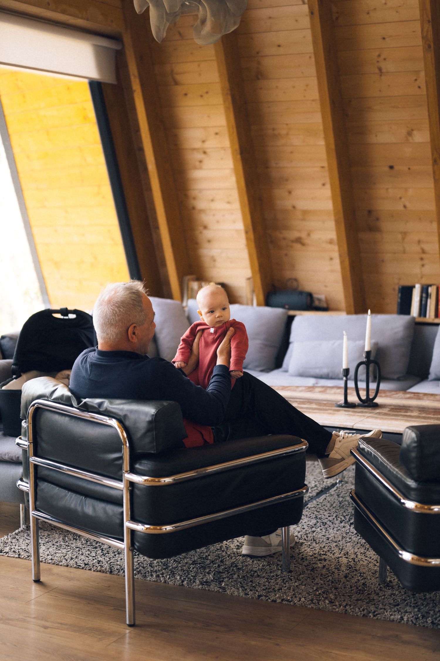 Man sitting in black leather chair holding a baby in a modern wooden cabin living room.