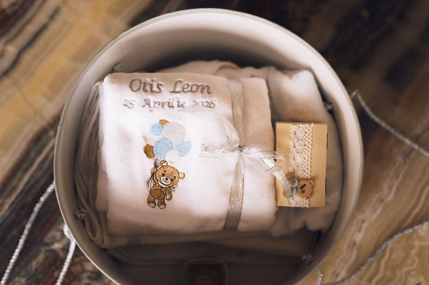 Personalized baby gift set with embroidered teddy bear onesie named Otis Leon in a white bowl.
